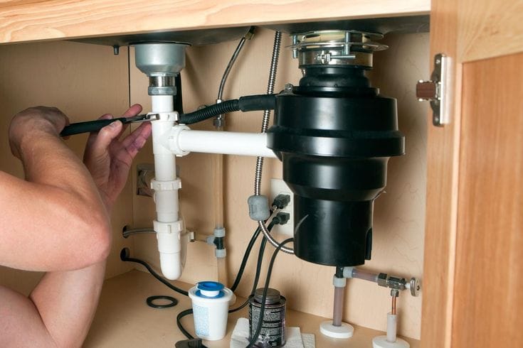 Plumber installing a garbage disposal beneath a kitchen sink in Winter Haven