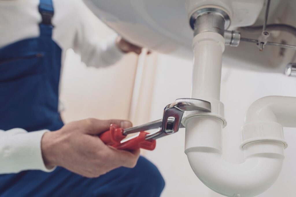 Plumber repairing a white drain pipe beneath a sink in Winter Haven